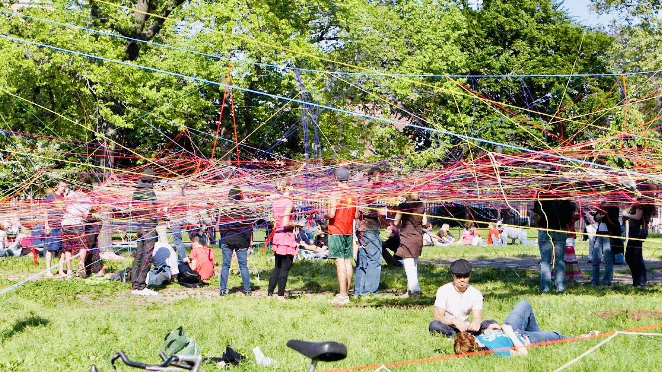 Crowds walking through a sprawling rainbow string installation at Copenhagen Metropolis Biennale