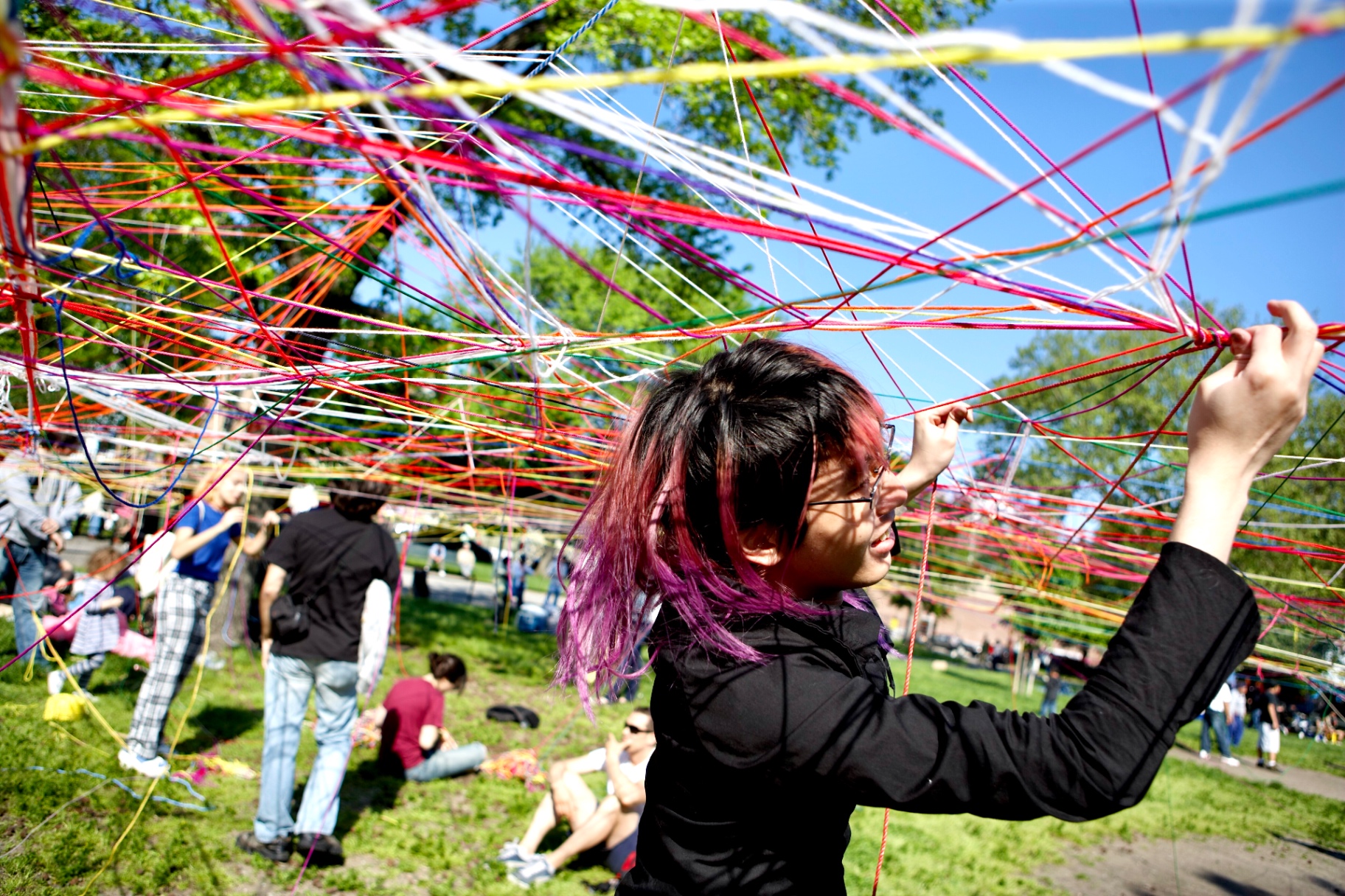 Pink-haired artist weaving colorful strings through the installation