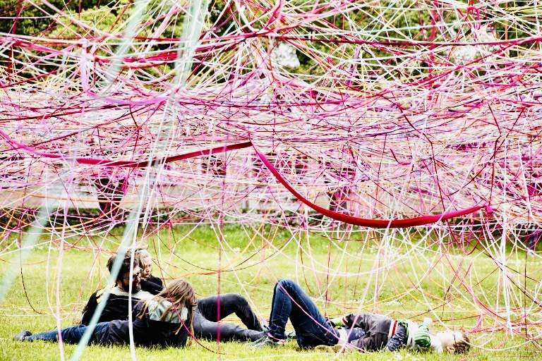 Families resting under a canopy of pink and red strings at Copenhagen Metropolis Biennale
